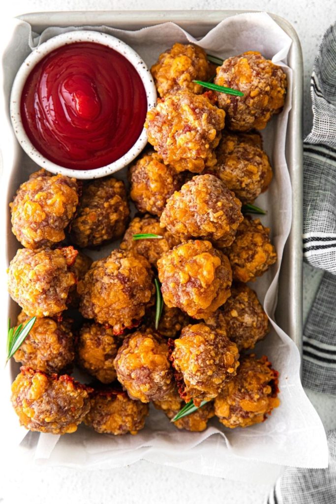 Overhead view of sausage cheese balls on a metal serving tray with dipping sauce.