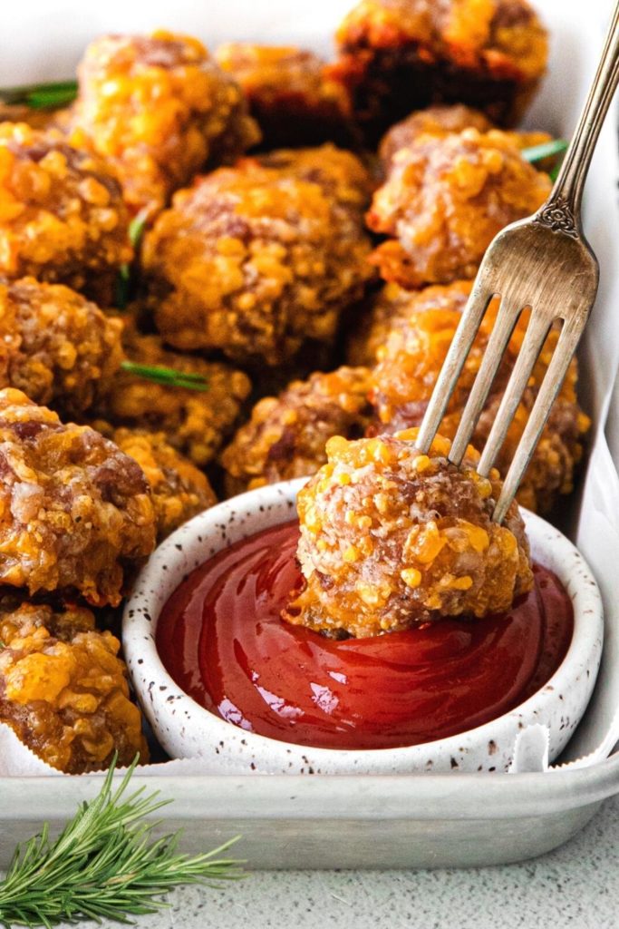Dipping sausage cheese ball appetizers into ketchup with a fork.