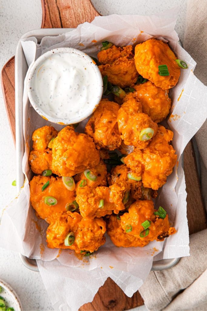 Buffalo chicken bites on a wooden appetizer board along with ranch dressing for dipping.