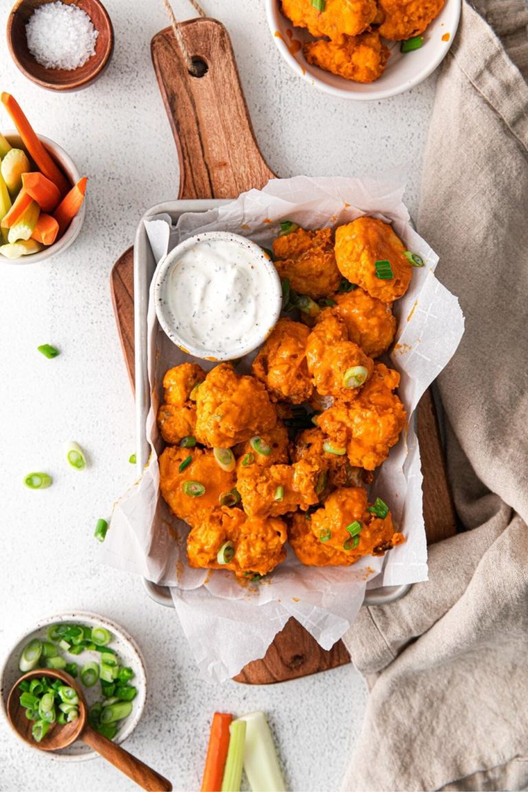 Buffalo chicken bites garnished with sliced green onions and served on a wooden board with ranch.