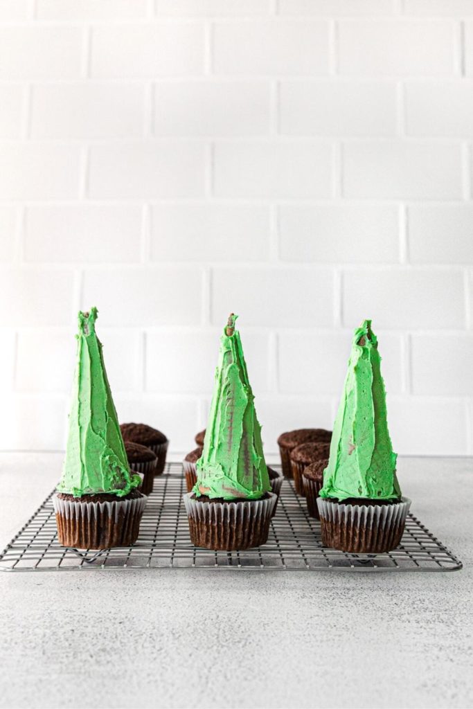 Three sugar cones with thin layers of frosting on top of 3 chocolate cupcakes.