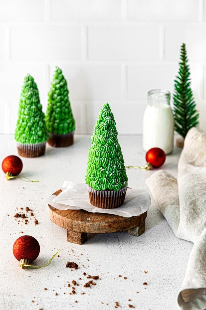 Three ice cream cone Christmas Tree Cupcakes on a holiday dessert table with milk.