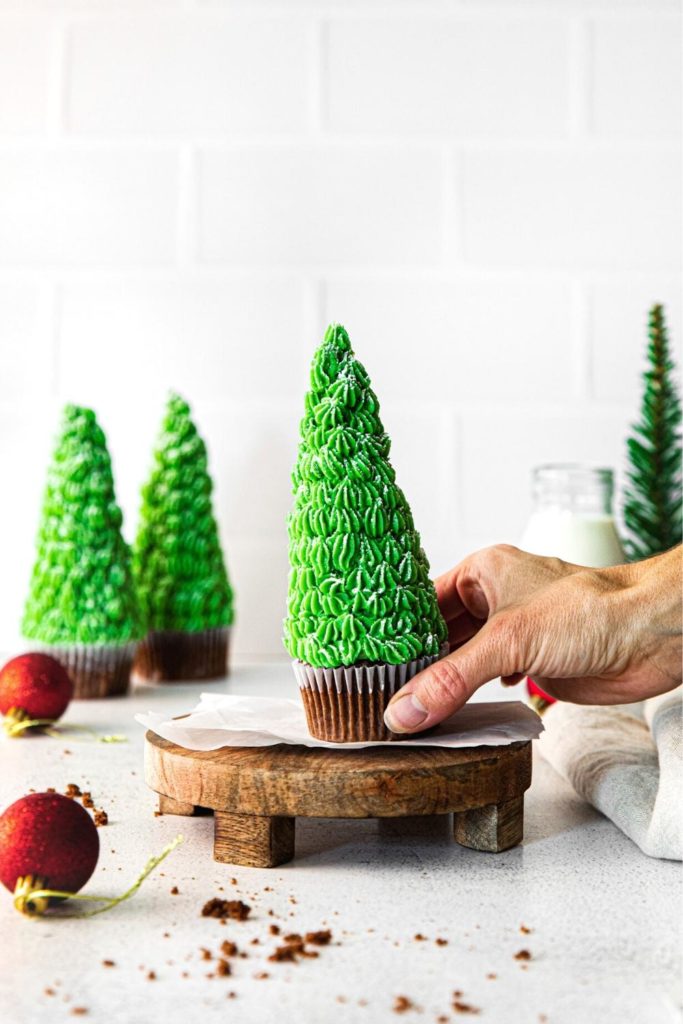 A Christmas Tree Cupcake being lifted off a wooden serving stand.