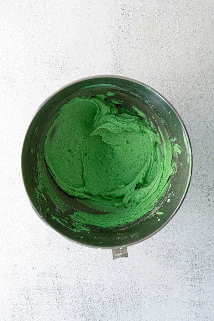 Vanilla buttercream frosting colored with green food gel in a metal mixing bowl.