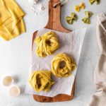 Three pasta nests assembled with authentic homemade pasta dough laid out on a wooden board.