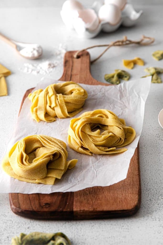 Fresh homemade pasta dough curled into 3 nests, set out on a wooden board.