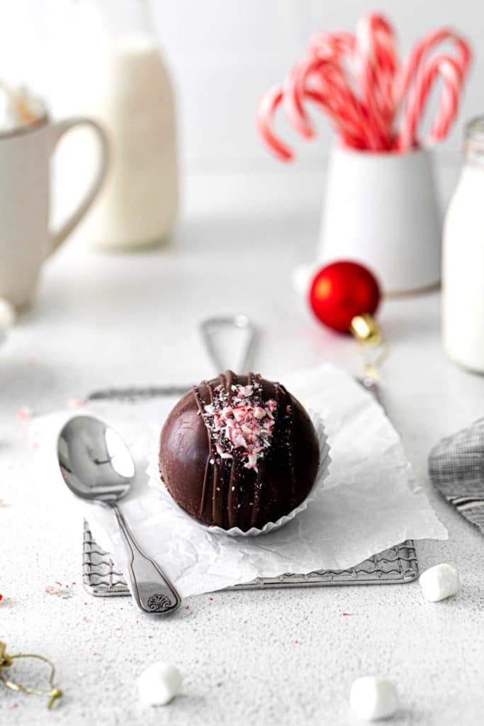 DIY peppermint hot cocoa bomb next to a mug on a Christmas dessert and drinks table.