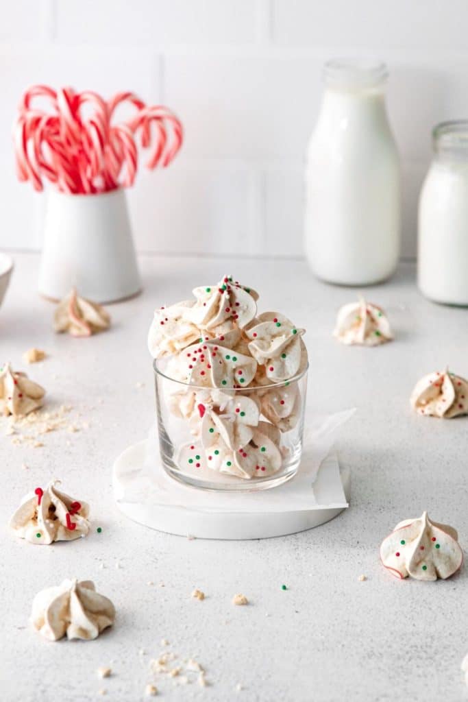 Peppermint Meringue cookies in a glass bowl alongside candy canes and milk on a Christmas dessert table.