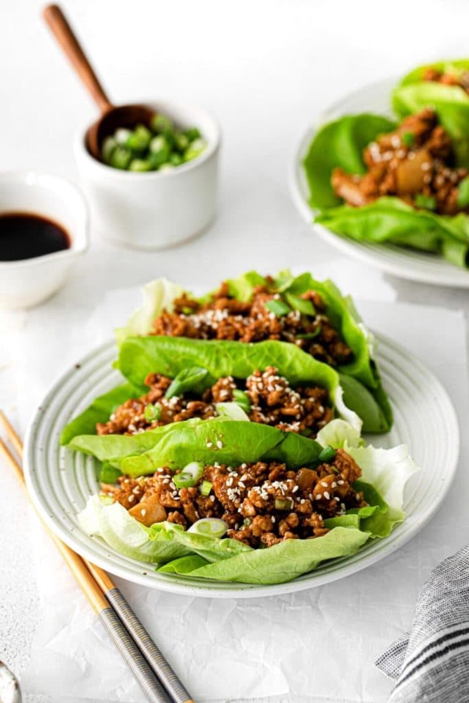 Healthy chicken lettuce wraps plated and garnished with sesame seeds and green onions served with chopsticks.