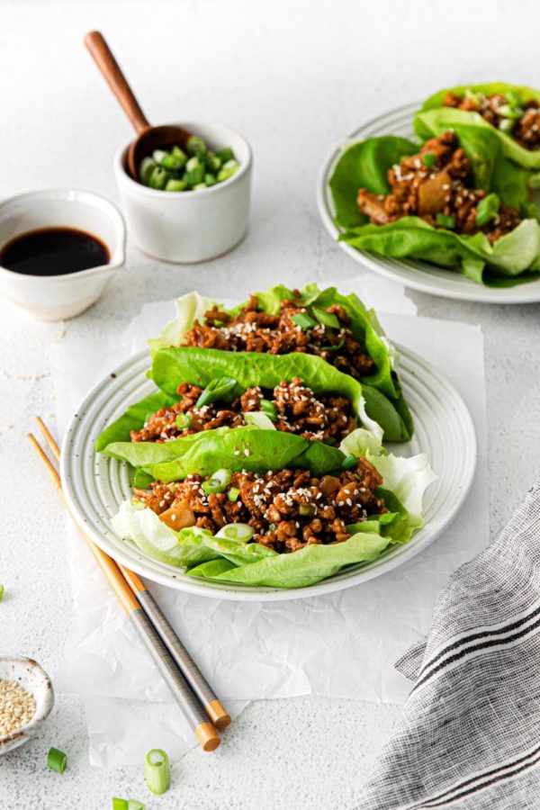 Copycat P.F. Chang's chicken lettuce wraps sprinkled with sesame seeds, served on 2 plates with chopsticks.