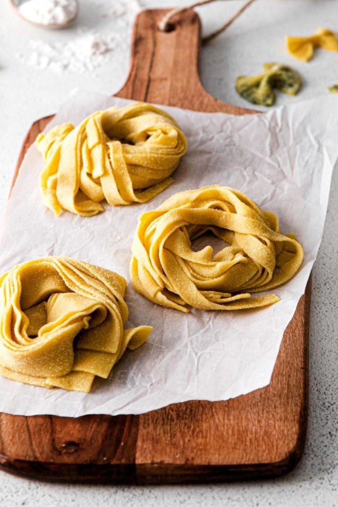 Sliced pasta gathered into nests on a parchment lined board.