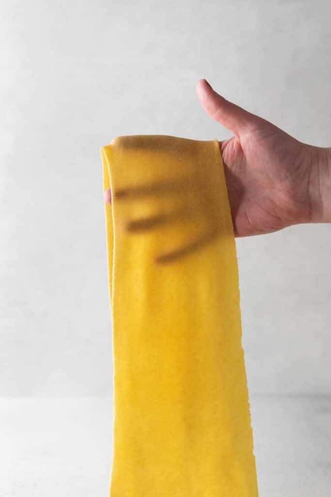 Holding a thin rolled-out piece of fresh homemade pasta ready to be sliced.