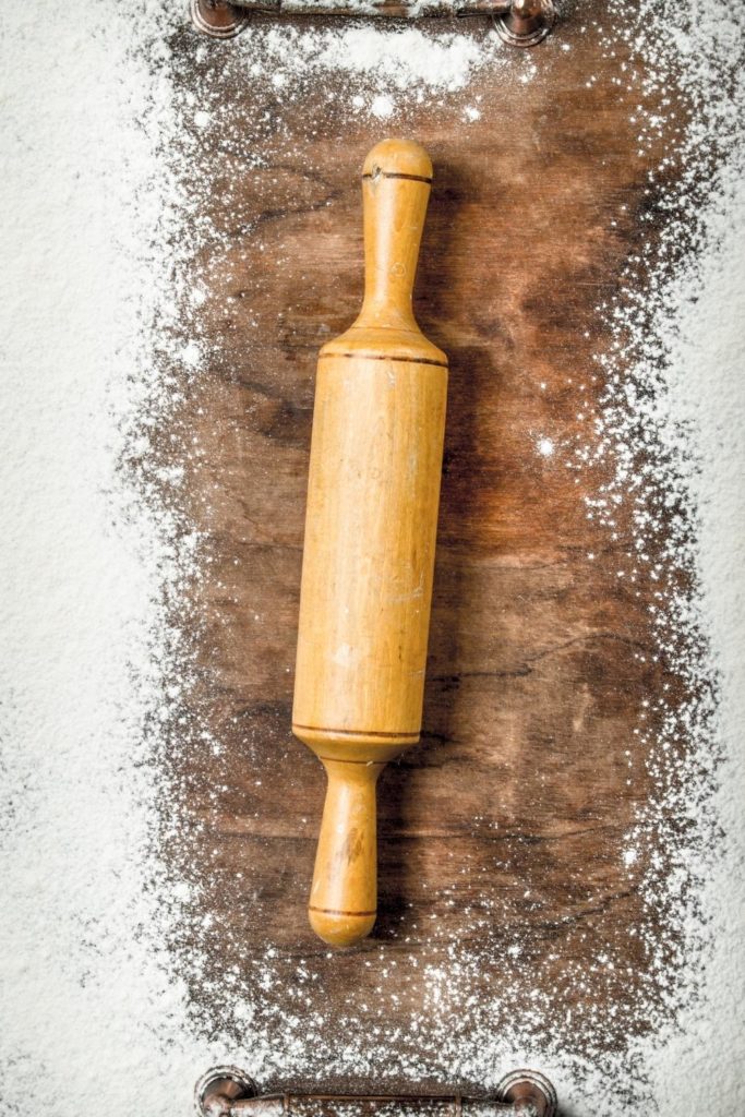 Wooden rolling pin atop a floured wooden board.