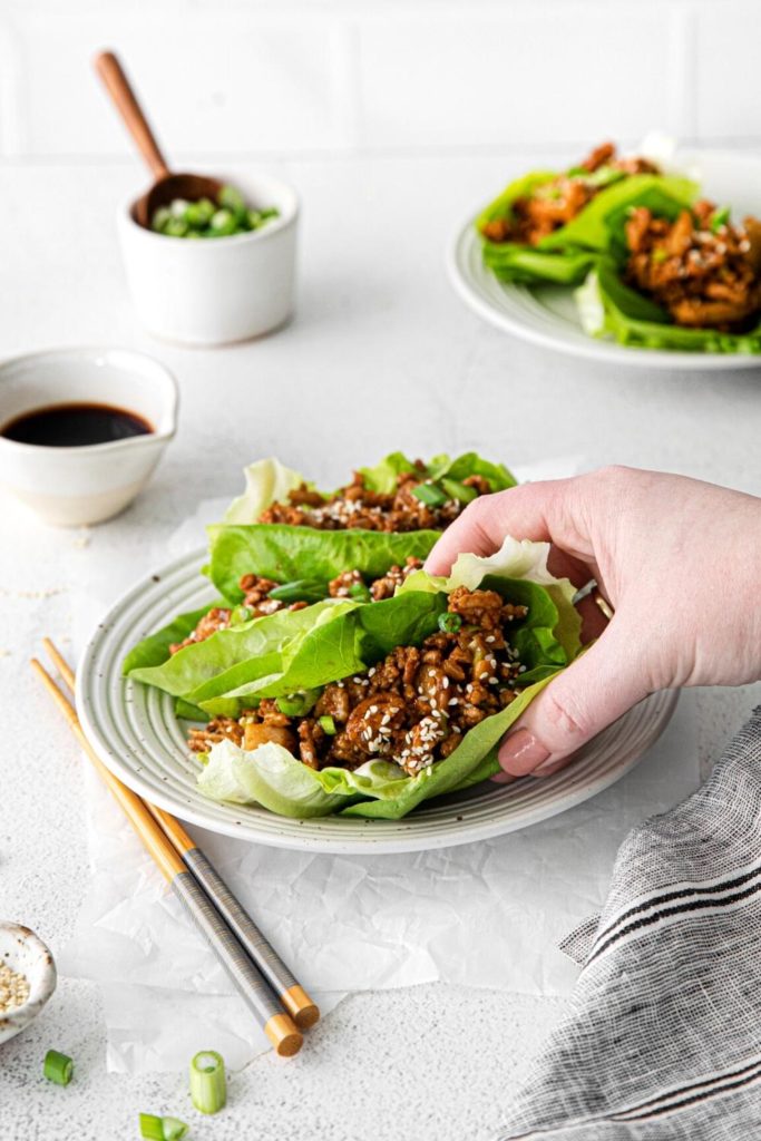 A hand grasping a chicken lettuce wrap off a plate at the dinner table.