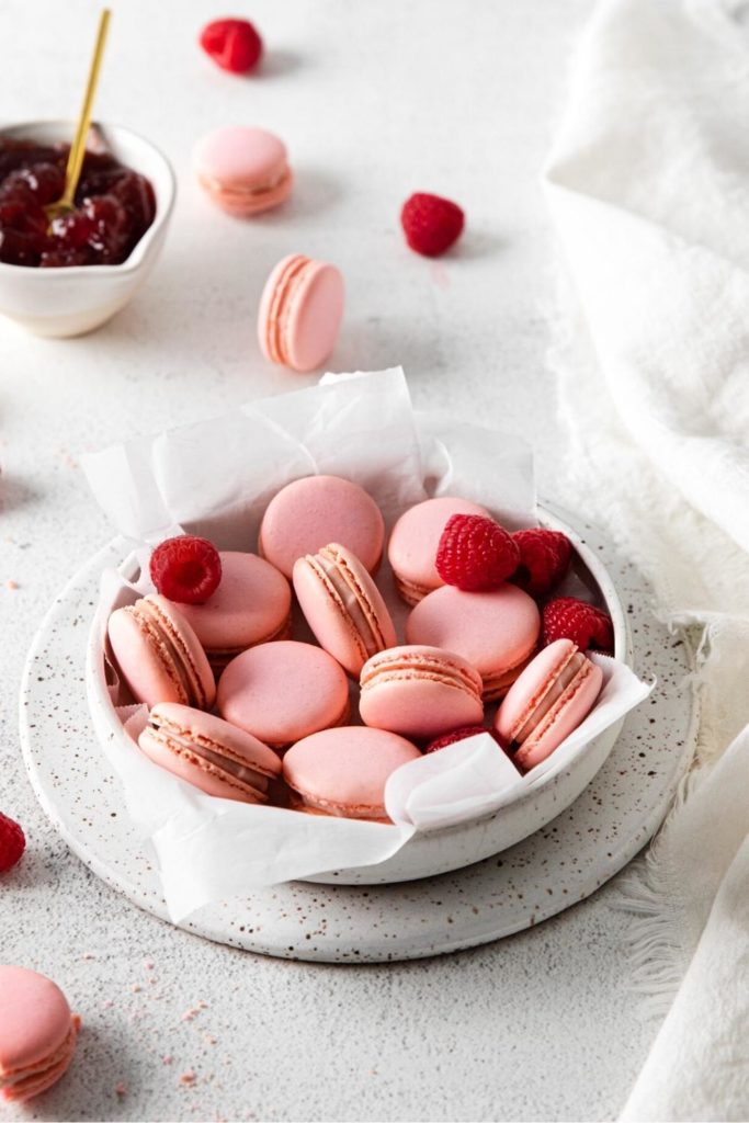 Pink Raspberry Macarons presented in a bowl with fresh raspberries for Valentine's Day.