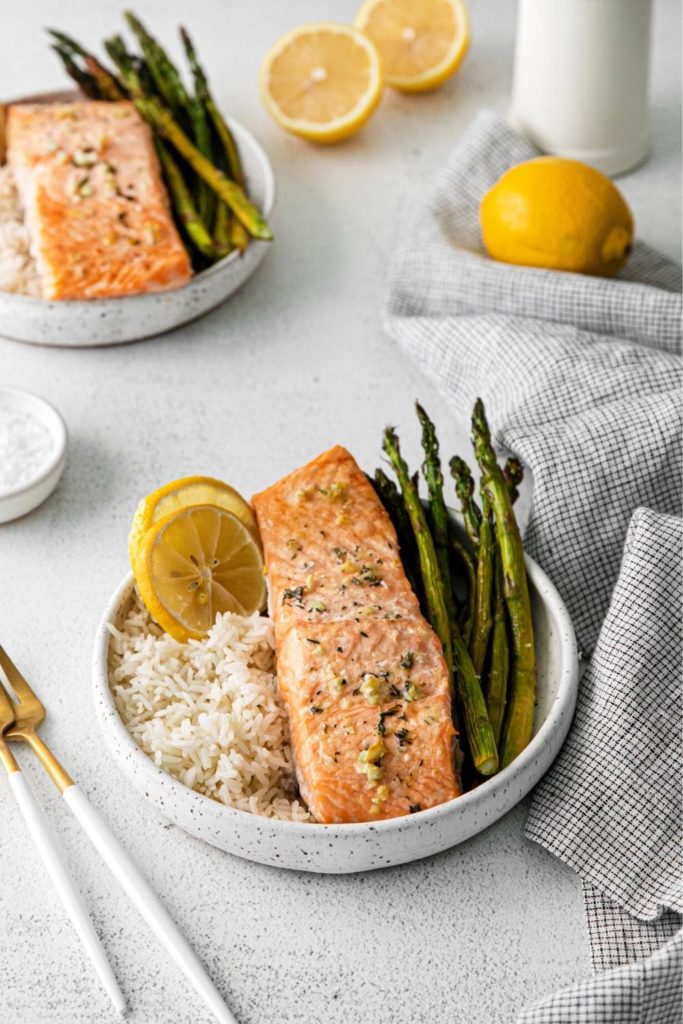 Lemon garlic butter salmon in a bowl with fluffy white rice, baby asparagus and lemon slices.