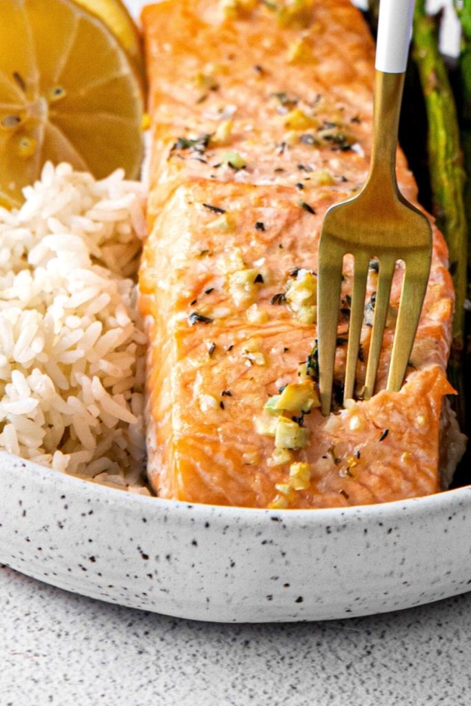 The tines of a fork digging into baked lemon garlic salmon and asparagus.