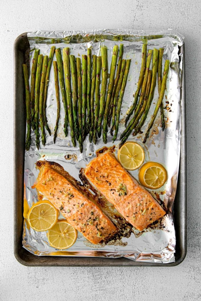 Baking tray with salmon asparagus sheet pan dinner, brushed with a garlic lemon-butter mixture.