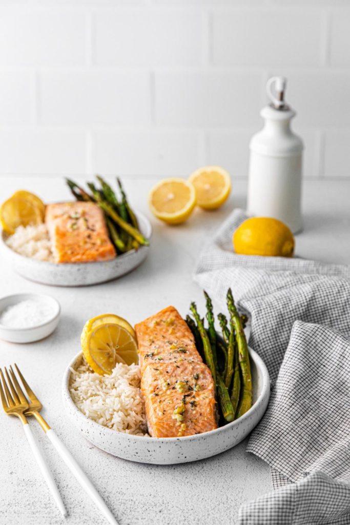 Baked lemon garlic-butter salmon served with asparagus and rice and slices of lemon.