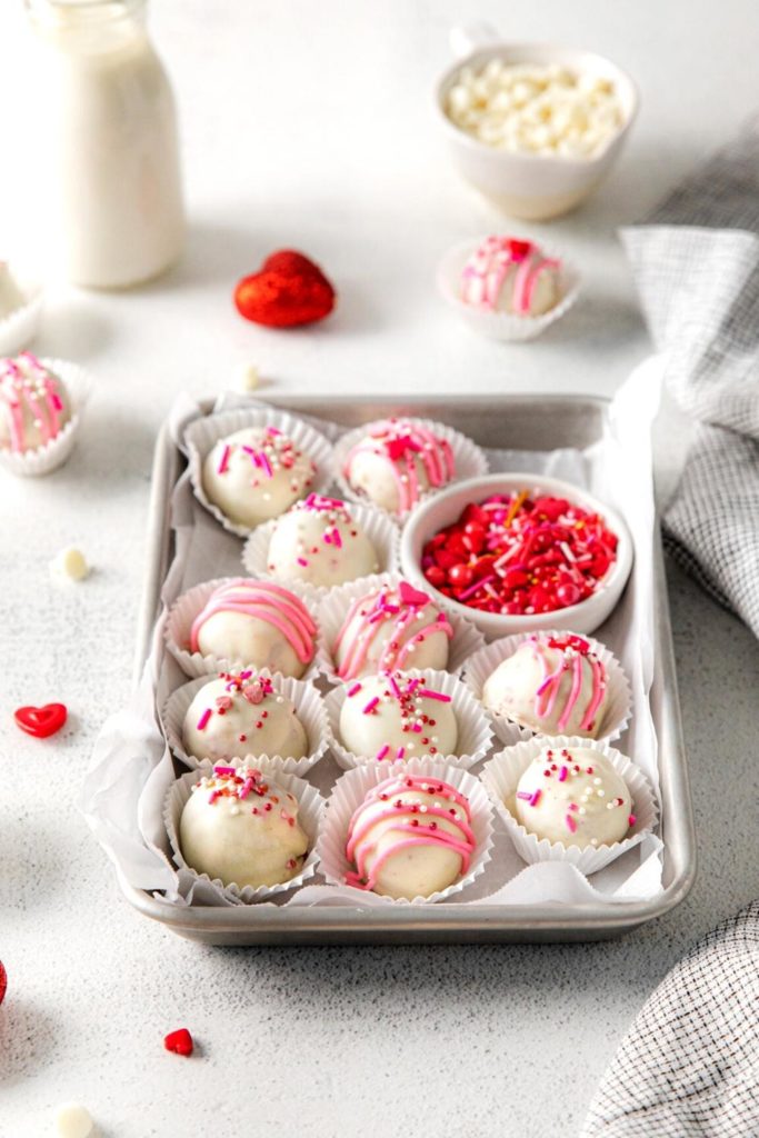 One dozen red velvet truffles in white paper candy cups arranged on a parchment-lined metal tray.
