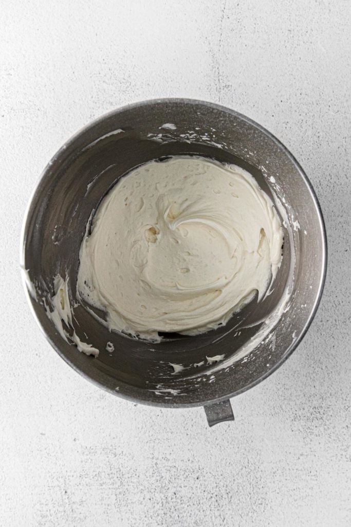 Metal bowl of a stand mixer with fresh, whipped, cream cheese frosting.
