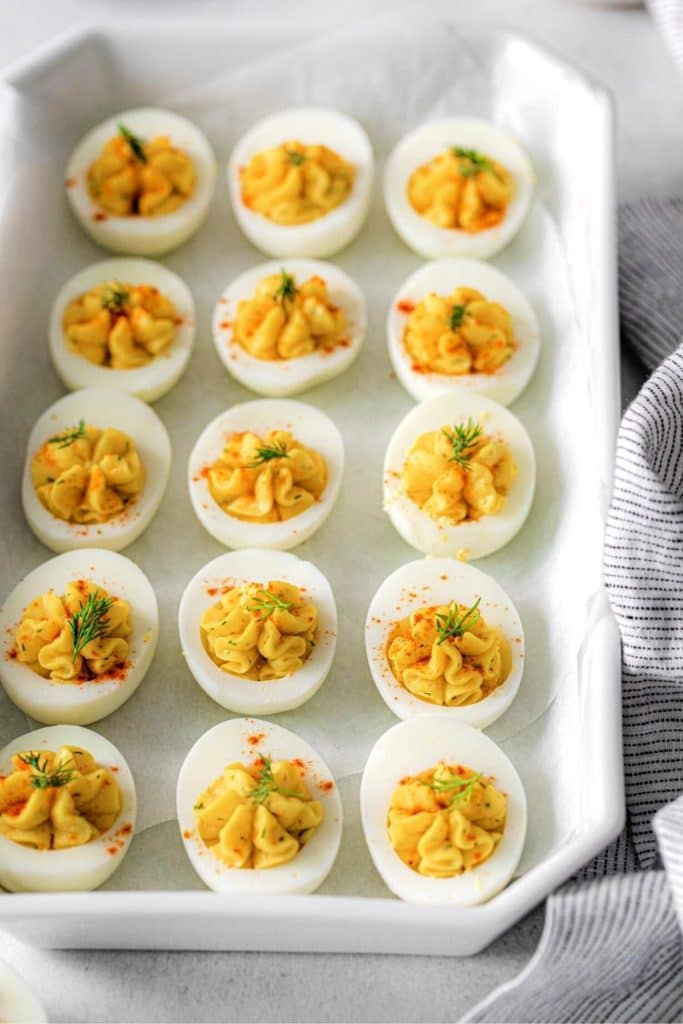 Twelve angel deviled eggs in a white ceramic dish on a serving table.
