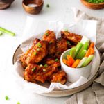 Baked BBQ Chicken wings served in bowl with sliced carrots and celery.