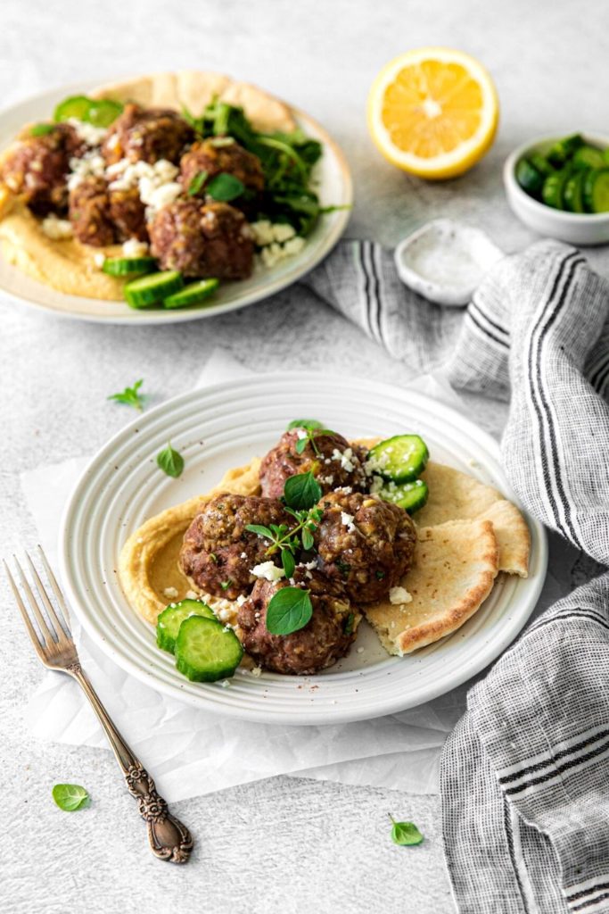 Baked Greek lamb meatballs on 2 dinner plates with fork.