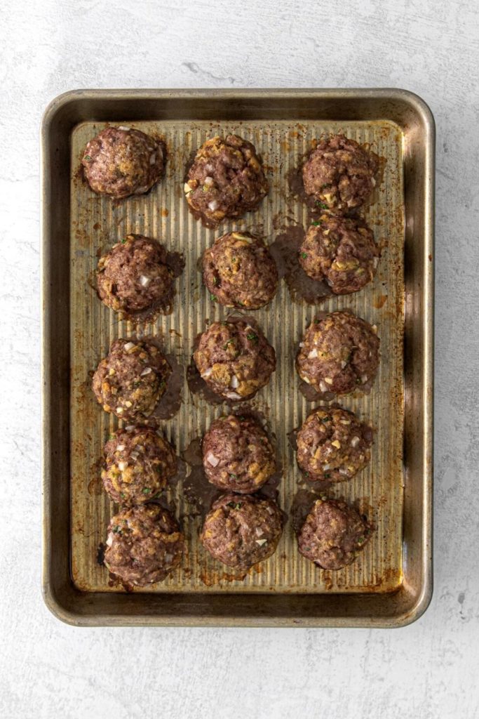 Fifteen oven-baked lamb meatballs on a small rimmed baking tray.