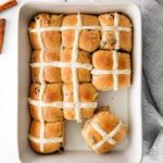Freshly-baked batch of hot cross buns on a serving table.