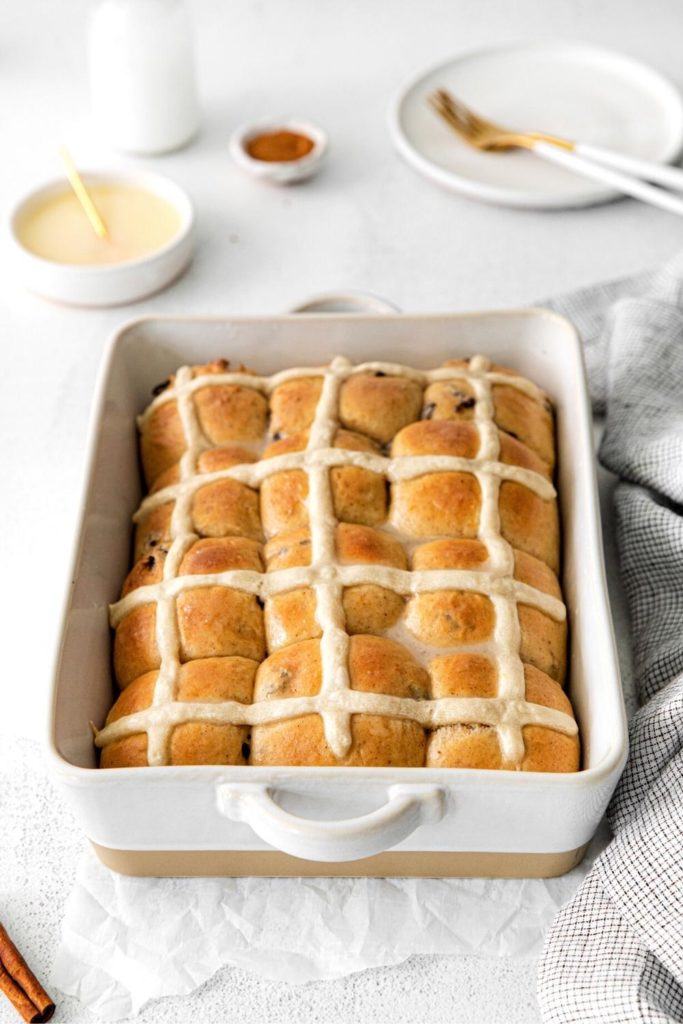 A ceramic baker with one dozen hot cross buns on a serving table.