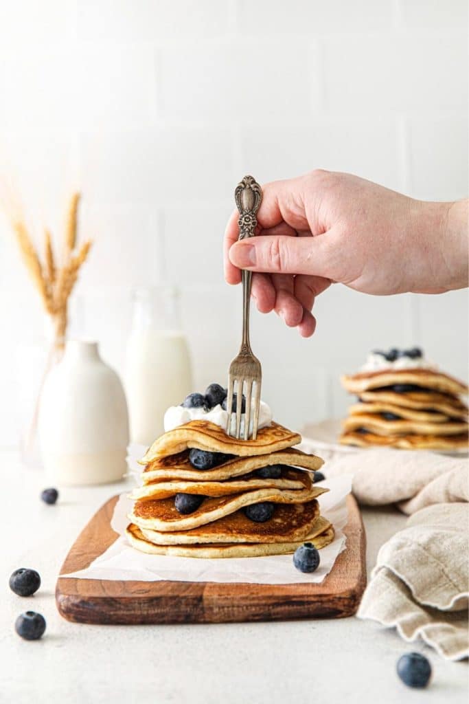 A fork digging into a stack of lemon blueberry pancakes.