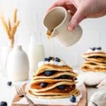 Maple syrup being drizzled over a warm stack of lemon blueberry hotcakes.