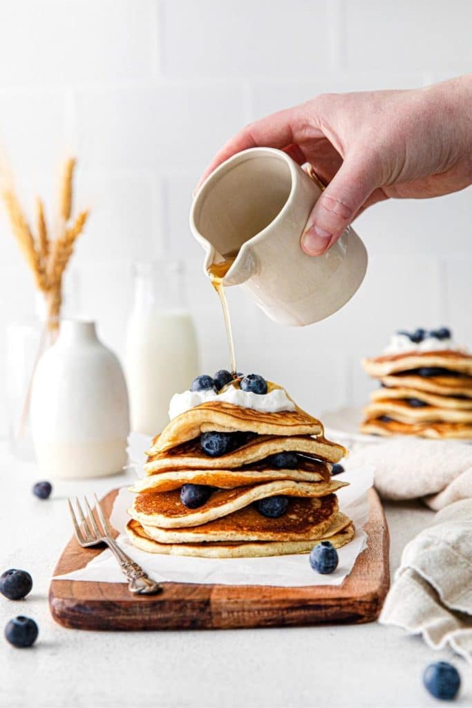 Pancake syrup being poured over the top of lemon blueberry pancakes.
