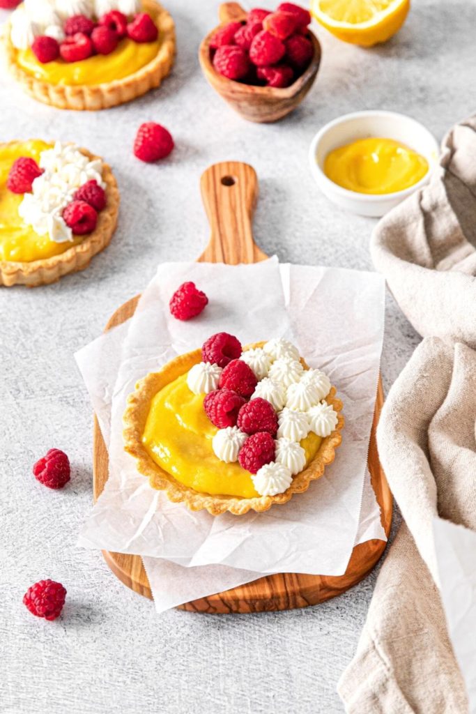 Mini Lemon Tarts garnished with whipped cream and fresh raspberries.