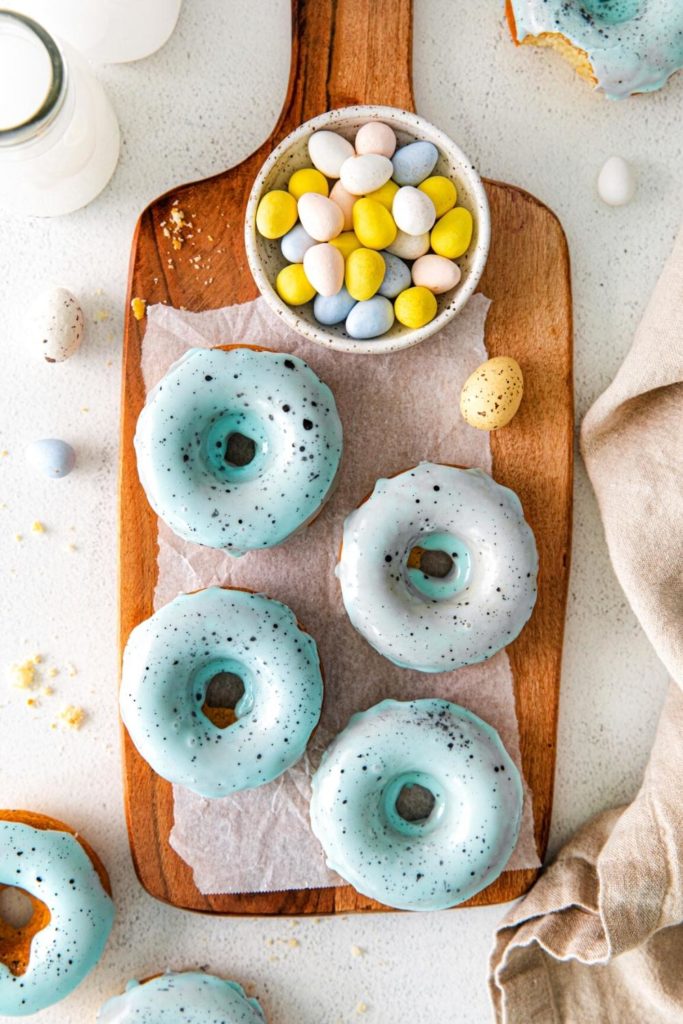 Baked Easter Egg Donuts being glazed with robin's egg blue colored icing with brown speckled spots.
