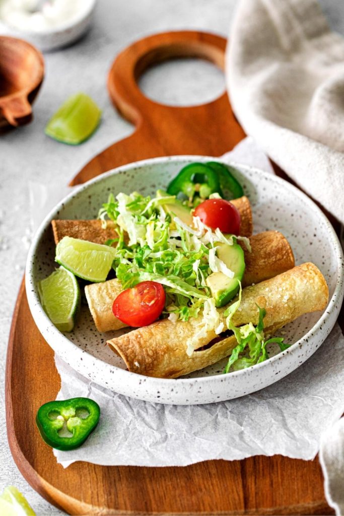Air fryer taquitos with chicken and cheese filling garnished with fresh produce.