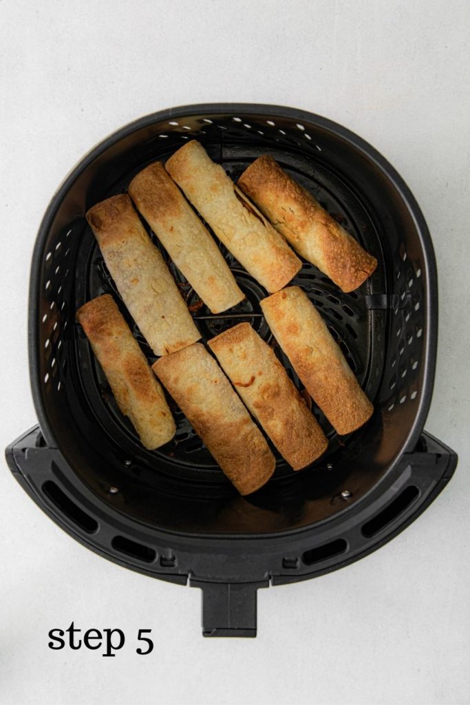 Cooked chicken taquitos in air fryer basket.