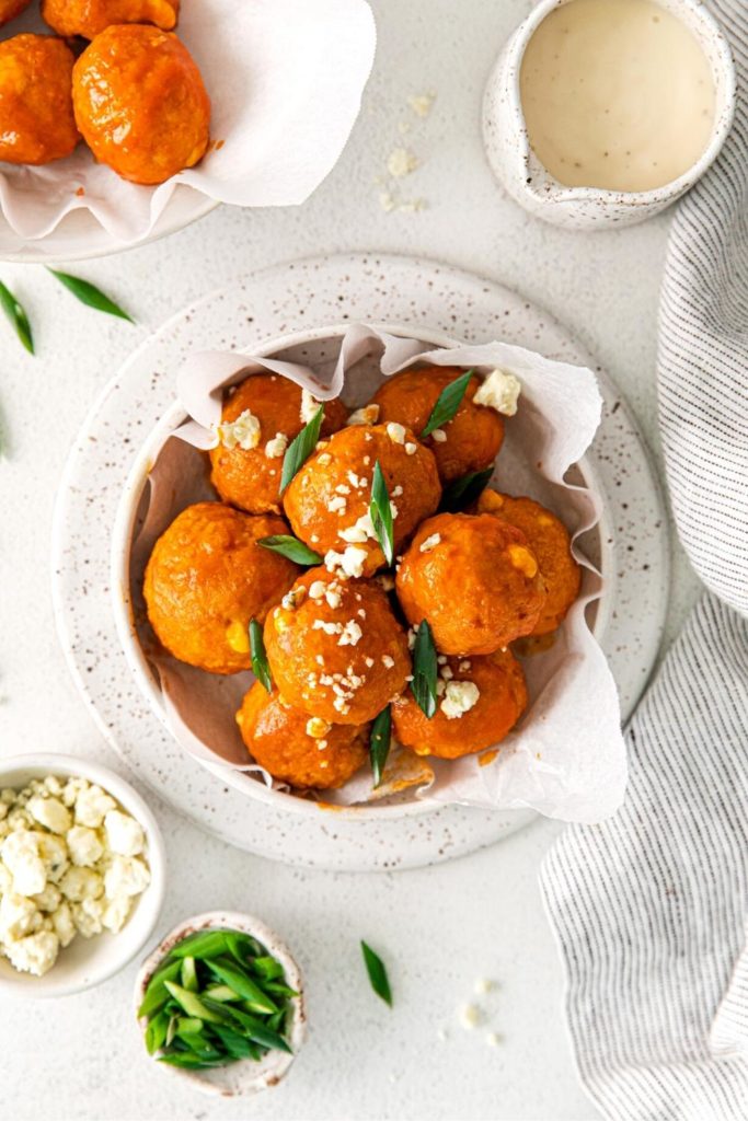 Overhead view of buffalo chicken meatballs with garnishes: crumbled cheese, green onions, ranch dressing.