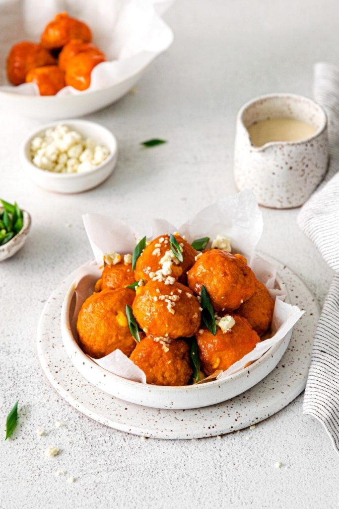 Buffalo Chicken Meatballs in a serving dish garnished with crumbled cheese and sliced green onion.