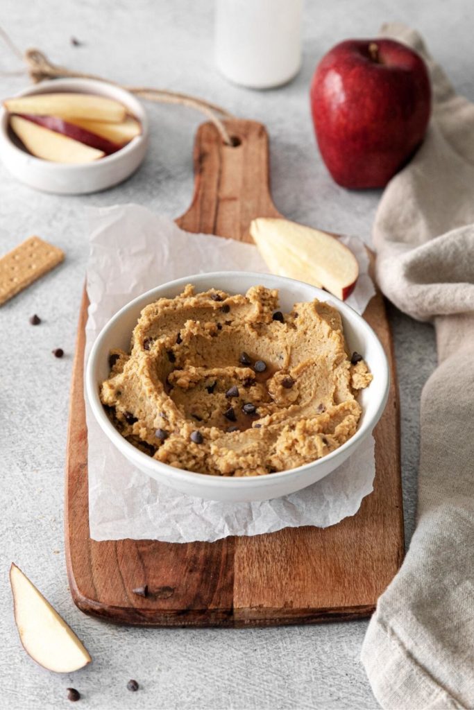 Chocolate chip cookie dough hummus on a serving table with apple slices and graham crackers.
