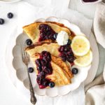 Plate of lemon blueberry crepes garnished with lemon slices and a dollop of whipped cream.