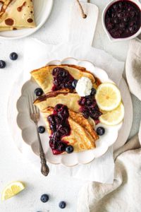 Plate of lemon blueberry crepes garnished with lemon slices and a dollop of whipped cream.