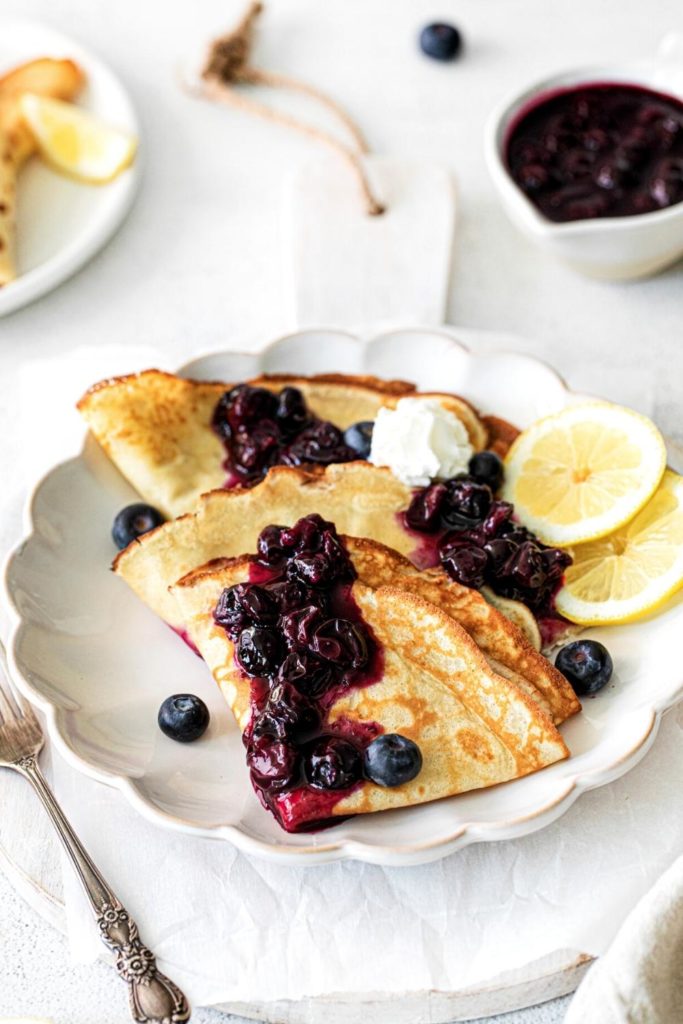 Blueberry crepes with fresh lemons and whipped cream on a plate with fork.