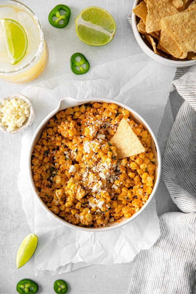 Bowl of Mexican street corn dip served with tortilla chips and wedges of lime.