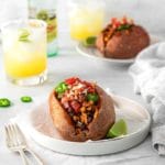 Loaded Mexican sweet potatoes on plates with taco toppings, served with Margaritas.