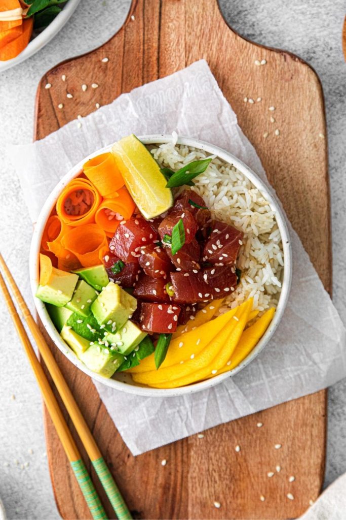 Overhead view of spicy tuna poke bowl on a wooden serving bowl with sesame seeds and chopsticks.