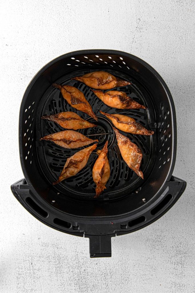 Air fryer basket with 9 cooked buffalo chicken wontons.