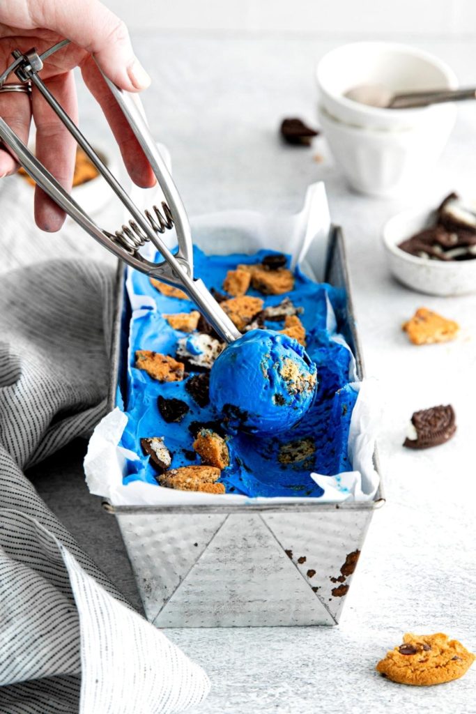 Metal scoop rolling out a serving of blue cookie monster ice cream from a metal pan.