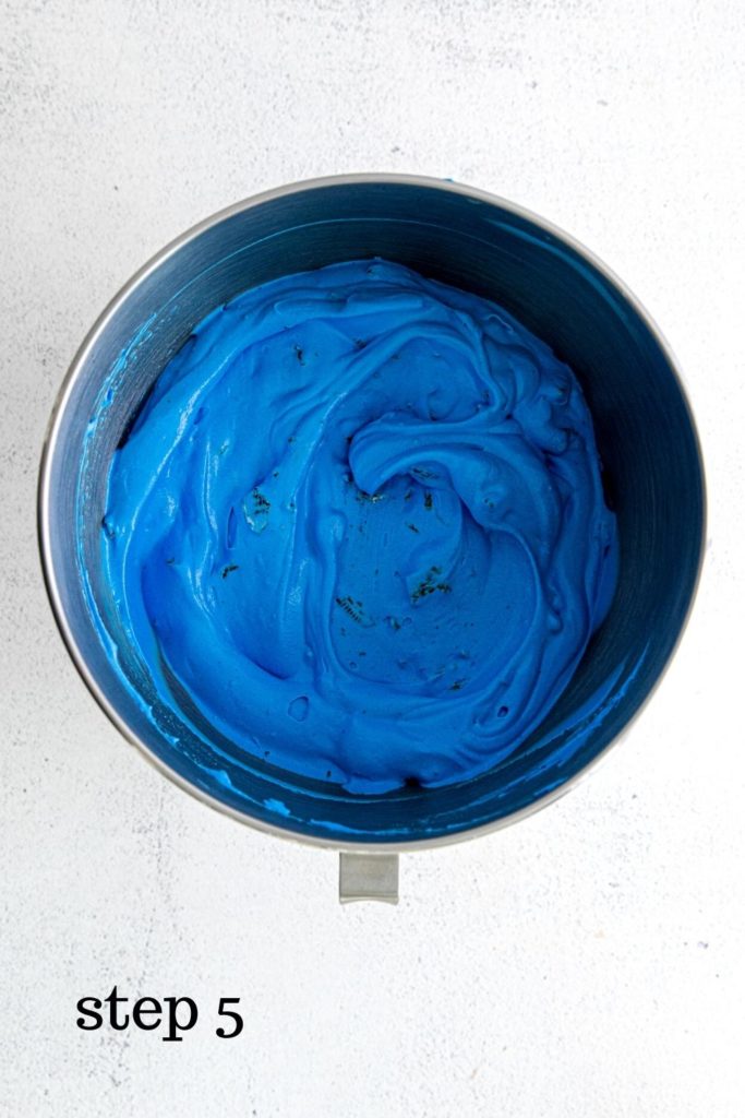 Oreos and Chip Ahoy cookies folded into blue ice cream in metal mixing bowl.
